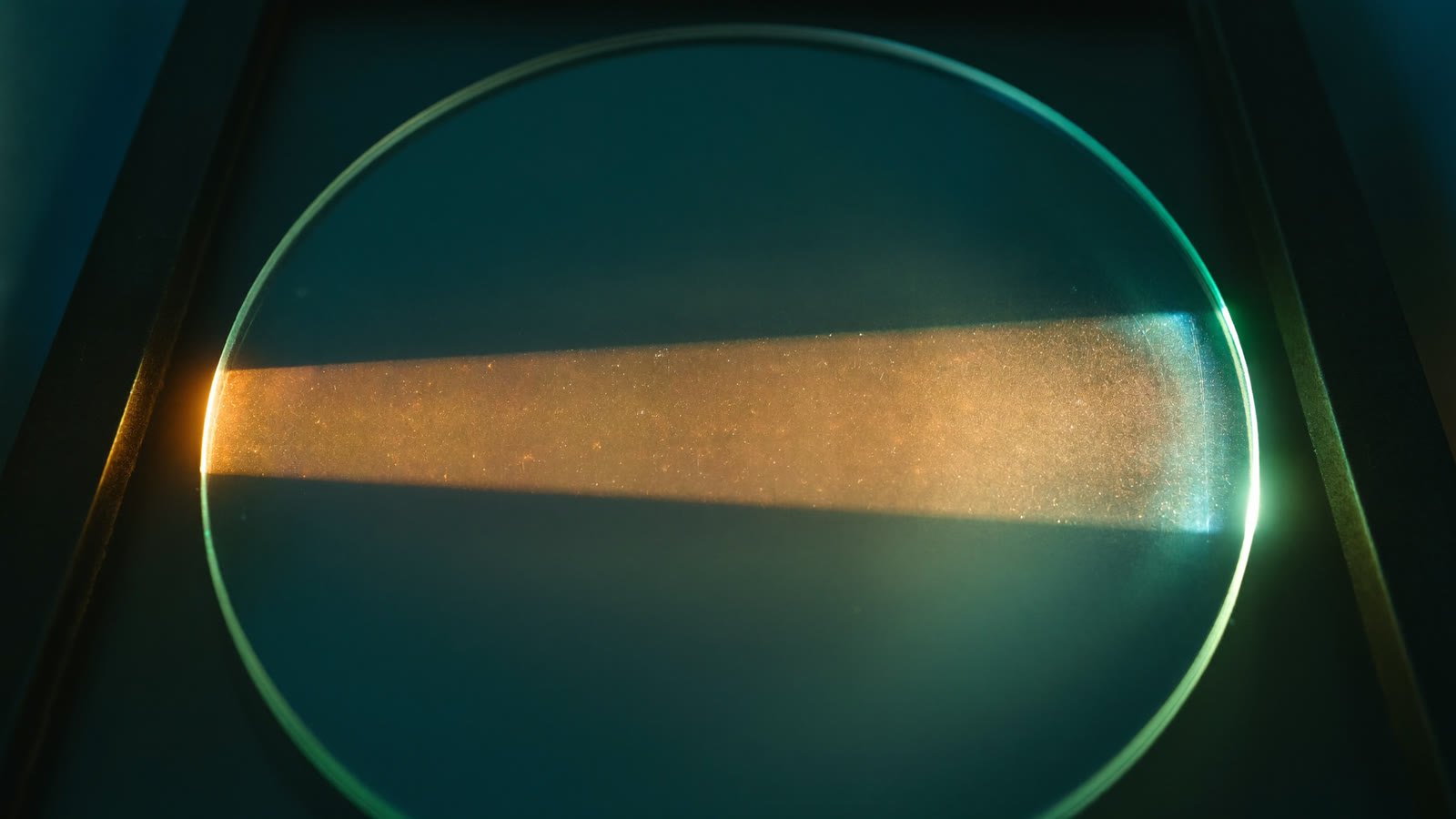 Ein warmer Lichtstrahl läuft quer durch eine runde Glasscheibe